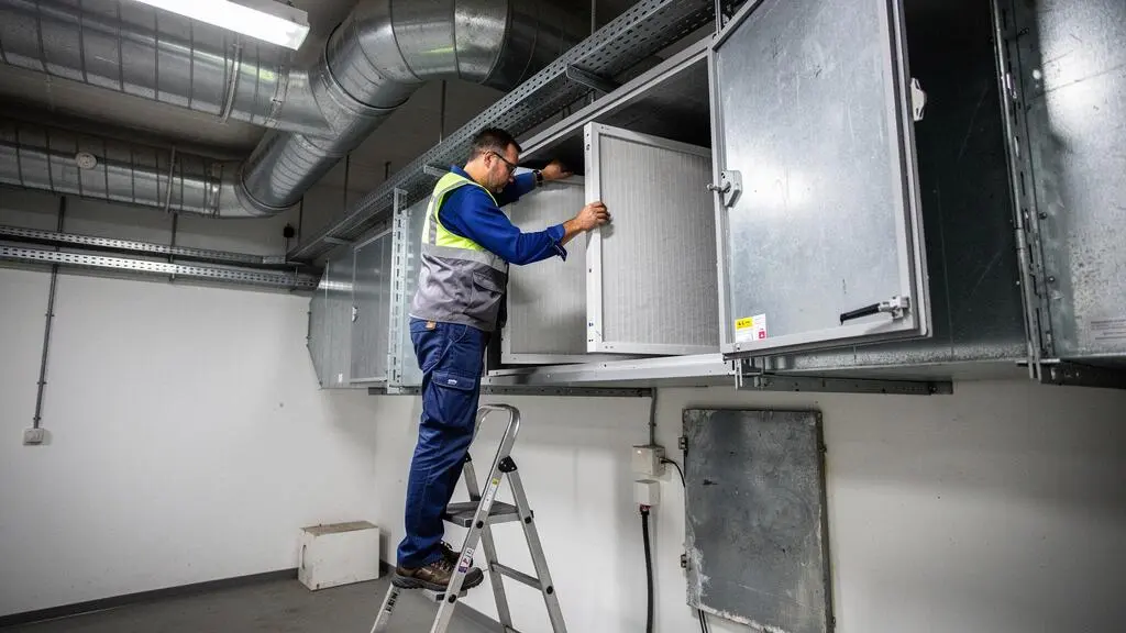 Technicien remplaçant un filtre dans un système de ventilation industrielle lors d'une opération de maintenance